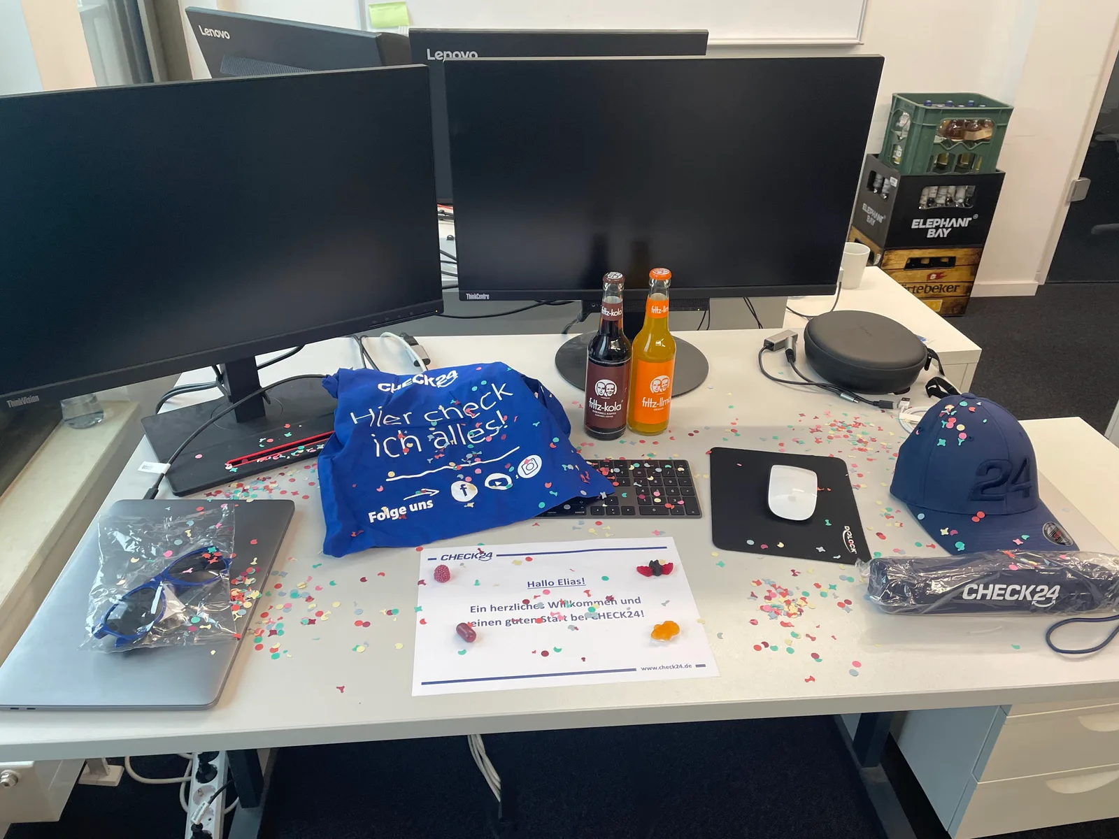 Desk with a CHECK24 welcome package, several monitors, and confetti